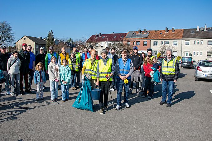 Eine Gruppe von Menschen, darunter Kinder und Erwachsene, steht für ein Gruppenfoto in einer Wohngegend. Sie halten Müllsäcke und tragen Reflektoren.