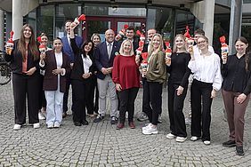 Eine Gruppe von Menschen steht vor einem modernen Gebäude und hält Getränke in der Hand.
