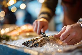 Person schneidet Fisch auf einem Bett aus Eis, dekoriert mit Lichtern.