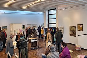 Eine Kunstausstellung mit Besuchern, die Gemälde betrachten und sich unterhalten.