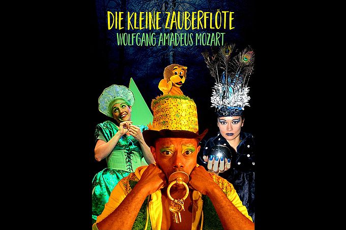 Ein farbenfrohes Plakat für Mozarts "Die kleine Zauberflöte" mit vier kostümierten Darstellern und einem Löwen-Puppenkopf.