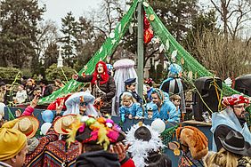 Eine bunte Karnevalsparade mit Menschen in Kostümen auf einem festlich geschmückten Wagen, die sich fröhlich verhalten.