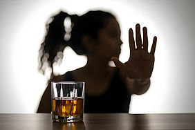 Silhouette einer Person mit abwehrend ausgestreckter Hand vor einem Glas mit bernsteinfarbener Flüssigkeit.