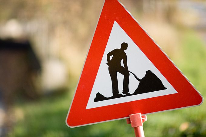 Ein Warnschild mit einem Mann, der mit einem Spaten arbeitet, auf rotem Dreieck.