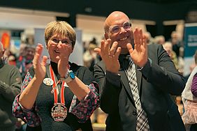 Zwei Menschen (Dagmar Andrae-Maukel und Bürgermeister Christian Horn-Heinemann) klatschen begeistert. Sie stehen in einer Menschenmenge.