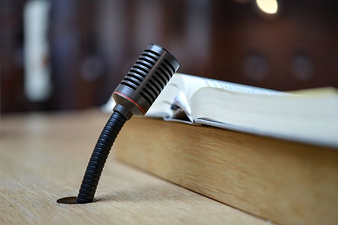 Ein Mikrofon steht auf einem Holztisch neben einem aufgeschlagenen Buch.