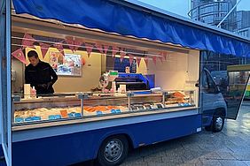 Ein blauer Lebensmittelwagen mit einem Verkäufer, der verschiedene Fischsorten anbietet.